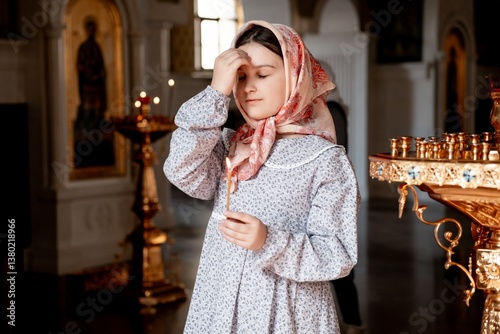 a child girl prays crossing herself in an Orthodox church holding a candle, a believing child