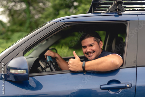 Positive middle-aged man gives a thumbs up while sitting in a small car, conveying approval, confidence, and a relaxed attitude.