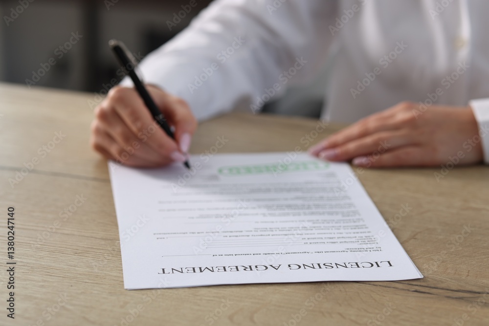 Woman signing licensing agreement document at wooden table indoors, closeup Woman signing licensing agreement document at wooden table indoors, closeup