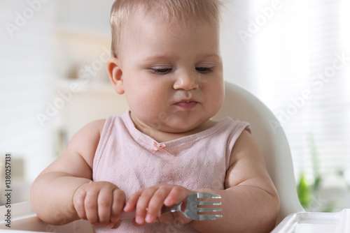 Obraz na plátně Cute little baby eating with fork on feeding chair at home