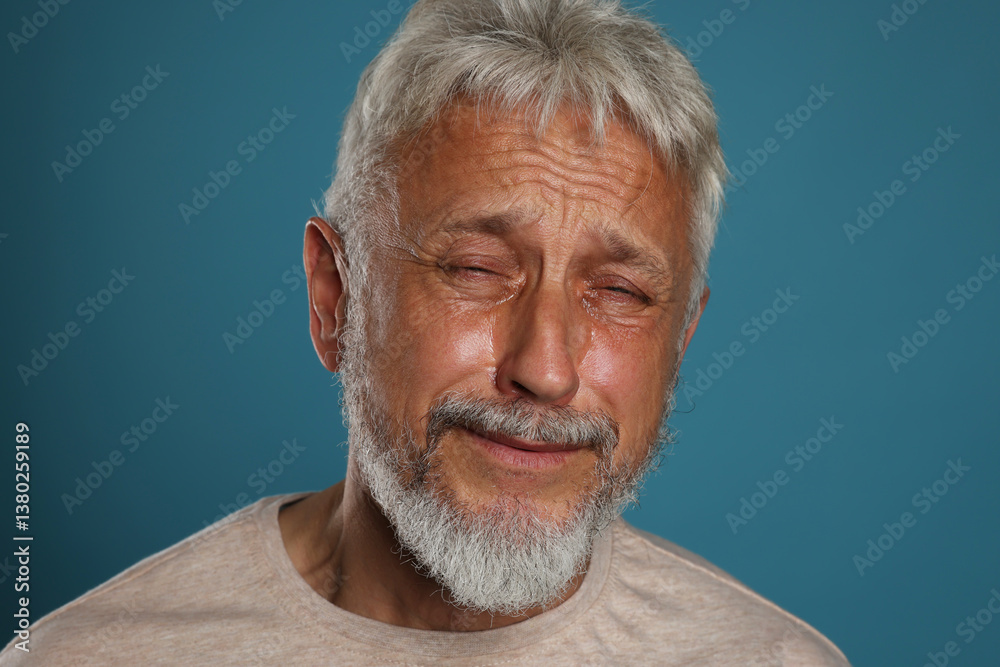 Sad senior man crying on blue background, closeup
