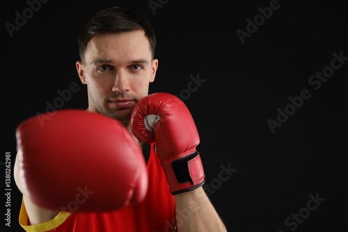 Man in boxing gloves fighting on black background, space for text