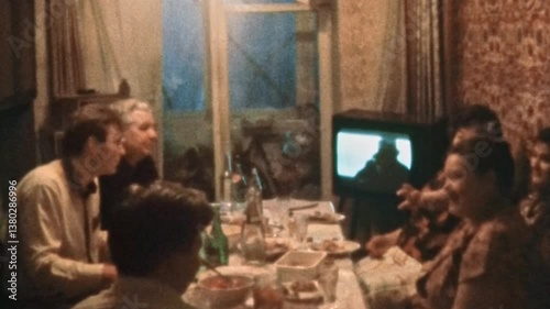 Large family having dinner in TV front at home indoor. Many people, smiling friends chatting, eating at dinner table together. Happy generation meeting. Vintage film. Retro archive. 1980s Ukraine 