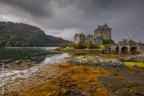 Obraz na płótnie Eilean Donan Castle stands majestically amid autumn hues, its reflection shimmering in calm waters. Misty Highlands and golden trees create a scene of timeless beauty. w salonie