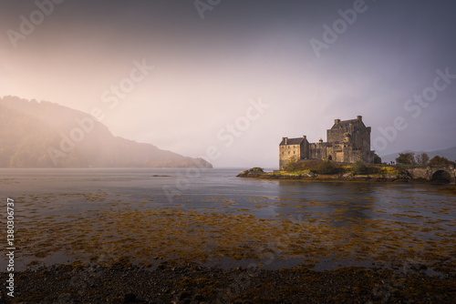 Obraz na płótnie Eilean Donan Castle stands majestically amid autumn hues, its reflection shimmering in calm waters. Misty Highlands and golden trees create a scene of timeless beauty. w salonie