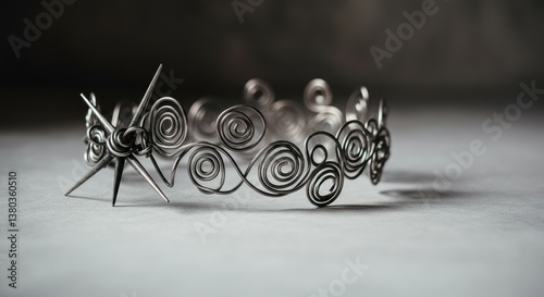 Intricate silver wire crown with spiral and star designs on gray surface