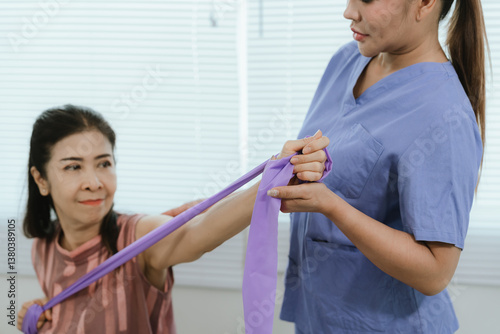 An elderly woman is assisted by a physical therapist to rehabilitate and stretch her arm during a treatment that focuses on physical rehabilitation, mobility and pain relief.