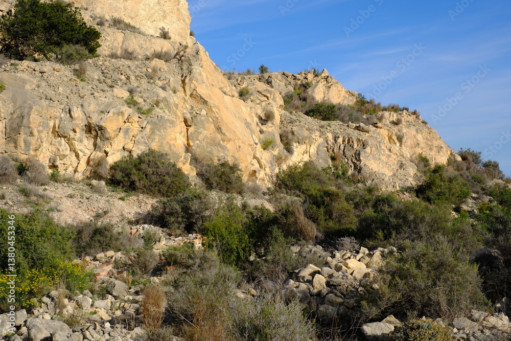 Rugged rocky hillside terrain with sparse vegetation and clear blue sky Rugged rocky hillside terrain with sparse vegetation and clear blue sky
