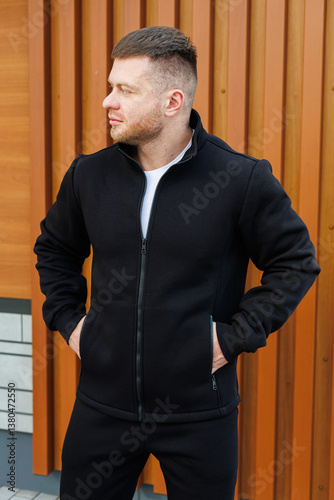Obraz na płótnie A stylish man, donned in a sleek black jacket, strikes a confident pose against a rustic wooden backdrop, fully embodying the essence of chic elegance and modern fashion sensibilities w salonie