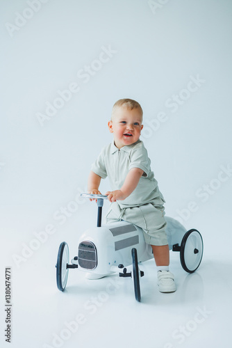 Obraz na płótnie An adorable toddler joyfully riding a classic toy car in a bright, minimalist studio setting, capturing the essence of carefree childhood adventure and vibrant imagination through playful exploration w salonie