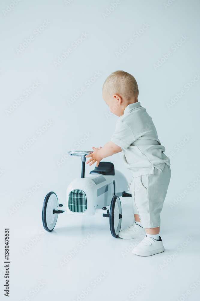 An adorable toddler, full of curiosity, is exploring a classic rideon toy car in a bright and cheerful studio setting, embracing the joy of childhood and the excitement of playful adventures