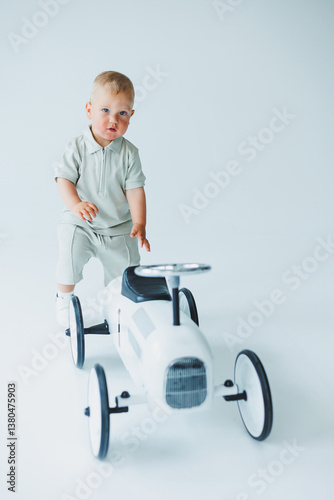 Obraz na płótnie An absolutely adorable toddler is having a wonderful time playing on a stylish toy car within a bright and cheerful studio environment, filled with light and color to stimulate creativity and joy w salonie