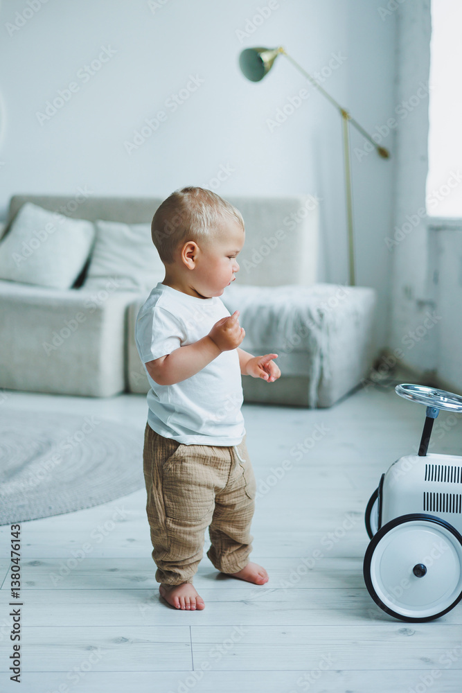 An adorable little toddler is joyfully exploring a modern living room while pushing around a colorful toy car, full of curiosity and playful energy, making the most of their cozy environment
