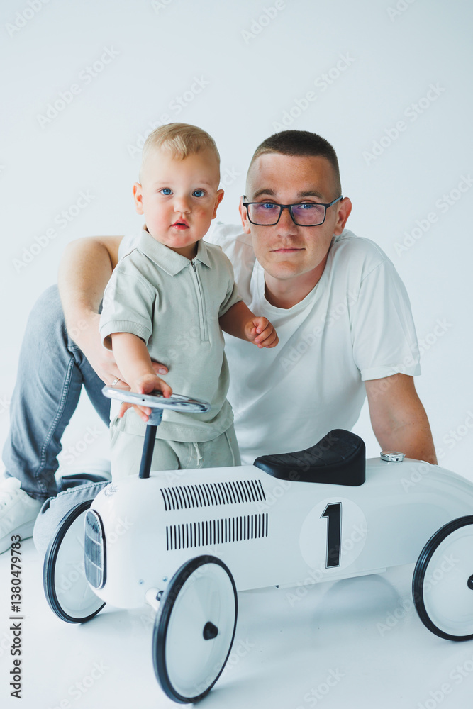 A Father and Child are enjoying a special bonding moment while playing together with a charming vintage rideon car, set against a modern studio backdrop that enhances their joyful experience