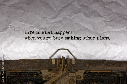 Life is what happens when you’re busy making other plans close up of a phrase being typed and centered on a sheet of paper on an old vintage mechanical typewriter.