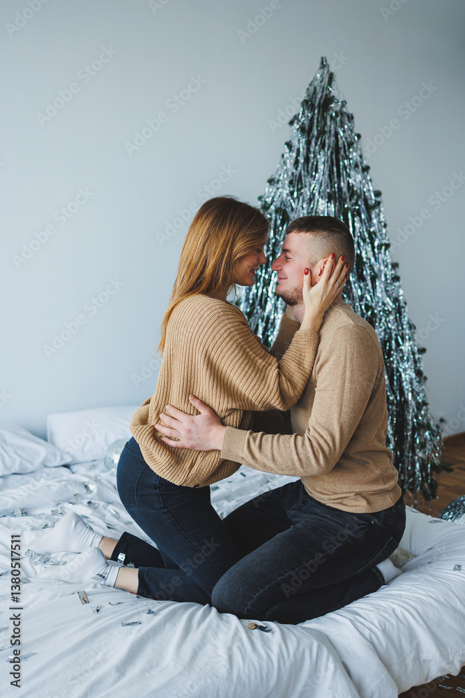 A Beautiful Romantic Moment A Young Couple Embracing Lovingly on Their Bed, Surrounded by a Festively Decorated Christmas Tree in a Cozy and Inviting Bedroom Setting, Perfect for the Holidays