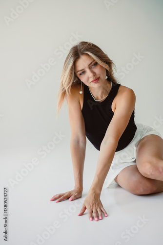 Obraz na płótnie A Stylish Young Woman Dressed in a Black Top, Posing Elegantly and Confidently on a Soft, Light Background, Radiating an Artistic and Playful Charm That Embodies Modern Fashion and Beauty w salonie