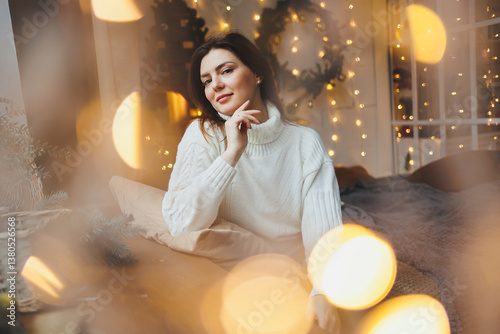 Obraz na płótnie Cute girl in New Year's locations in a cozy living room. Woman at home for the new year. w salonie