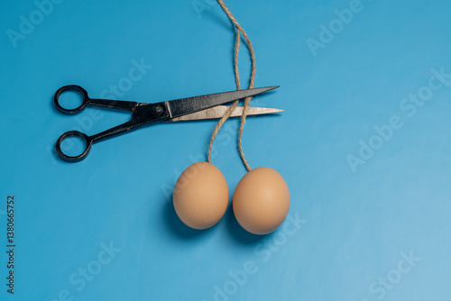Foto Doctor uses scissors to cut the rope that holds two eggs on a blue background, close up