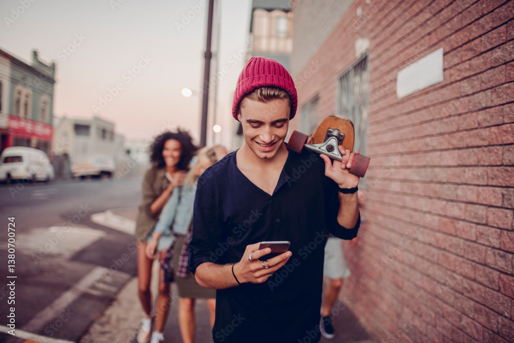 © Marko Geber - Young skater guy smiling at phone while walking with friends on city street