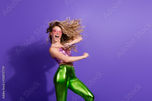 Happy young woman in shiny outfit dances against vibrant purple background, exuding fun and energy photo