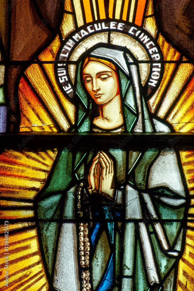 Fototapeta premium Stained glass of Apparition of the Virgin Mary, Our Lady of Lourdes or Notre Dame de Lourdes to Bernadette Soubirous.