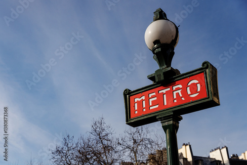 Fototapeta Naklejka Na Ścianę i Meble -  A red and white sign with the word Metro written on it. The sign is on a green pole. The sky is blue