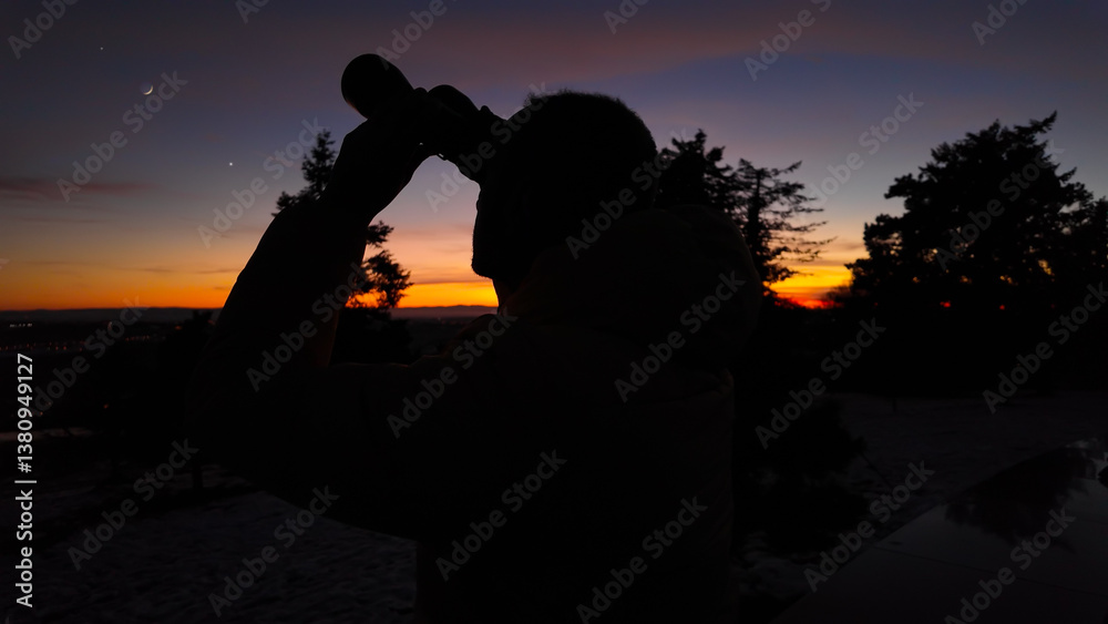 Amateur astronomer looking at the evening skies, observing planets, stars, Moon and other celestial objects with binoculars.