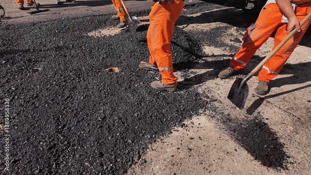 Construction workers working on a new asphalt layer on a public street.