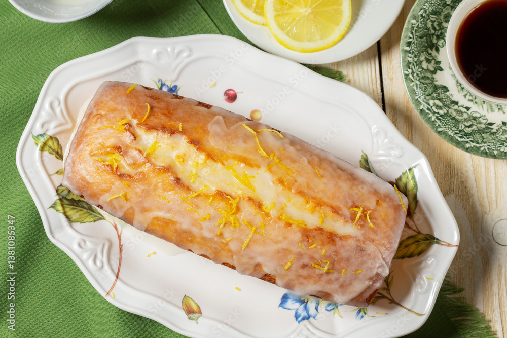 Aromatic lemon cake, covered with sugar icing and sprinkled with zest, served with tea.