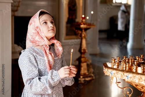 a child girl prays crossing herself in an Orthodox church holding a candle, a believing child