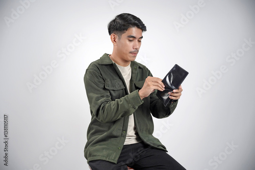 Young Asian man shocked while looking at his wallet in casual shirt looking at empty wallet, having financial problems isolated on white background