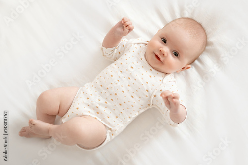 A newborn baby is lying on the back and smiling on a white bed in the bedroom, a happy cute little baby, top view. Place for the text