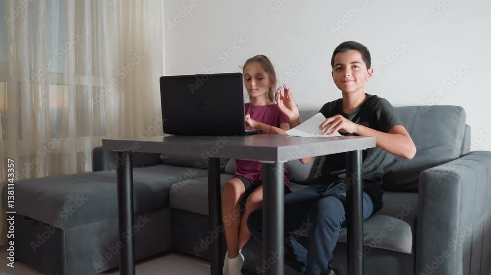 young boy finishes writing assignment in living room and shows work to someone while his sister watches attentively beside him at table with laptop during homework session young boy finishes writing assignment in living room and shows work to someone while his sister watches attentively beside him at table with laptop during homework session