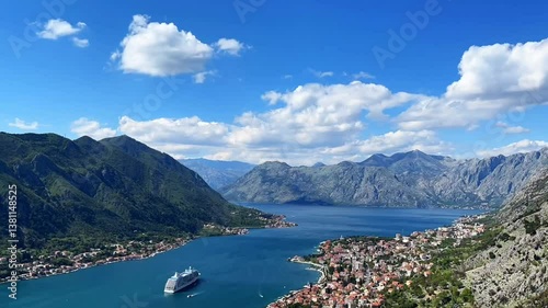 A cruise ship sails through the breathtaking Bay of Kotor, Montenegro, surrounded by majestic mountains, deep blue waters, and historic coastal towns under a vivid sky.