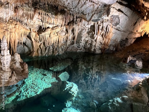A breathtaking view of an underground emerald lake inside a cave, surrounded by stunning stalactites and water basins.