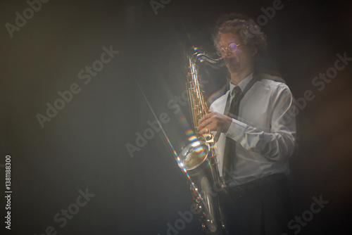 Motion blur shot of adult male saxophone player in white shirt improvising on wind instrument creating unique riff and melody in studio with black backdrop, light refraction effect