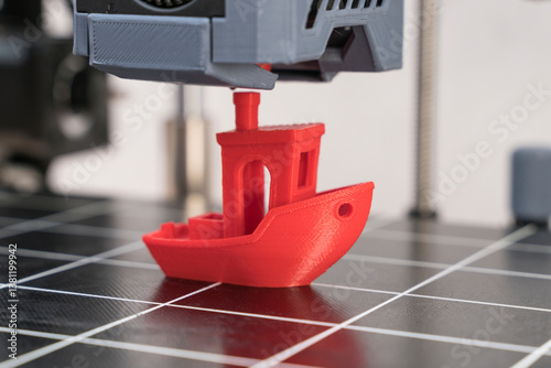 Red 3D printed boat is created on a printing bed with precise layer formation in a modern workshop