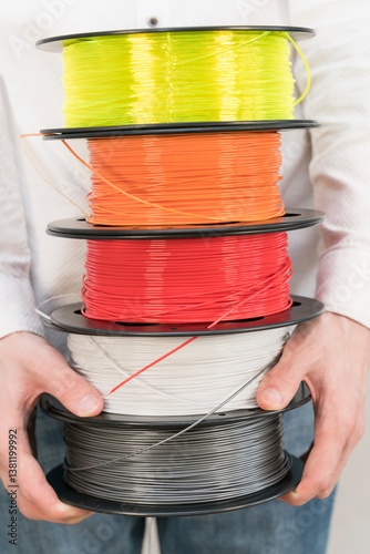 Caucasian man holds a stack of plastic filament spools for 3D printing.