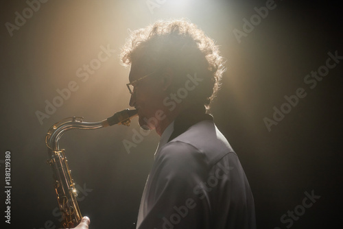 Photos Side view shot with backlight of adult curly man improvising on saxophone playin