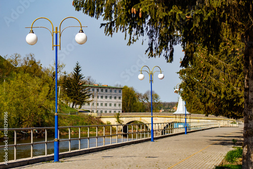 Fototapeta Naklejka Na Ścianę i Meble -  A bridge over a river next to a tree and street lights