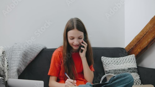 Teenager enjoying a call while studying at home with laptop and notebook in cozy living room setting