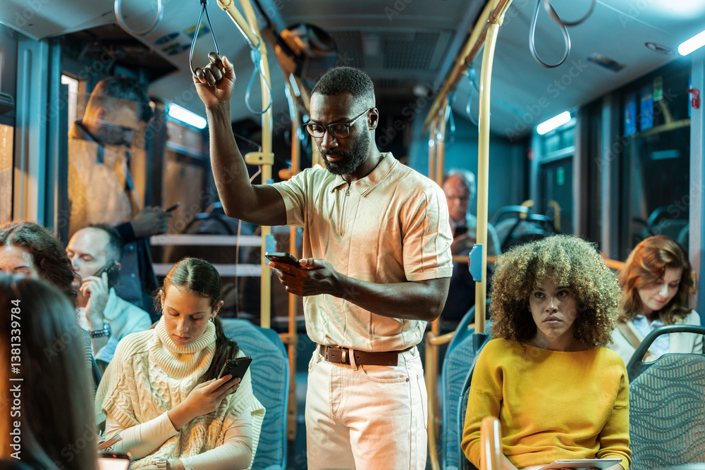 Fototapeta premium Young man using smartphone while standing on a crowded bus