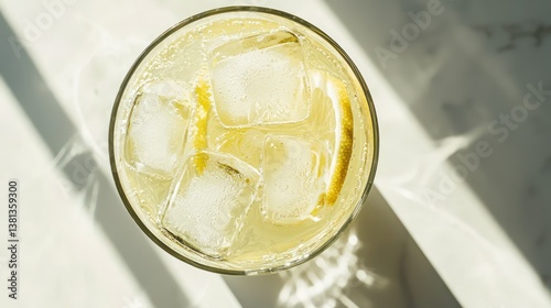 A refreshing summer beverage, a zesty lemon drink with ice cubes, bathed in sunlight on a marble surface.