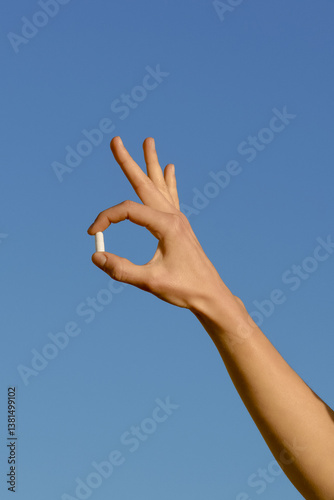 Vertical image of a female hand holding a white pill against a blue sky background. Concept of health, medicine, treatment of diseases and depression