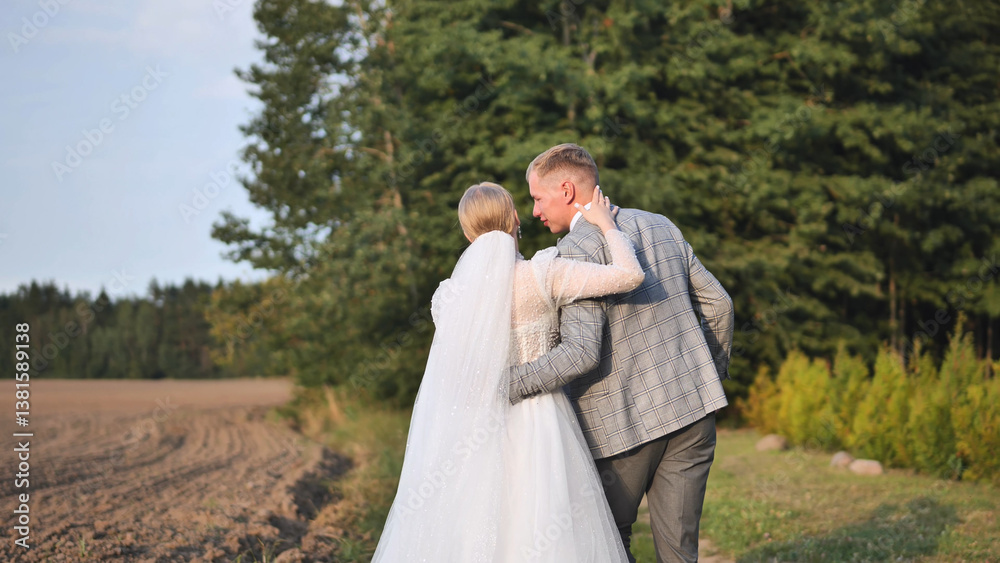 Newlywed couple strolling together, holding hands in sunlit meadow, sharing intimate wedding day moment Newlywed couple strolling together, holding hands in sunlit meadow, sharing intimate wedding day moment