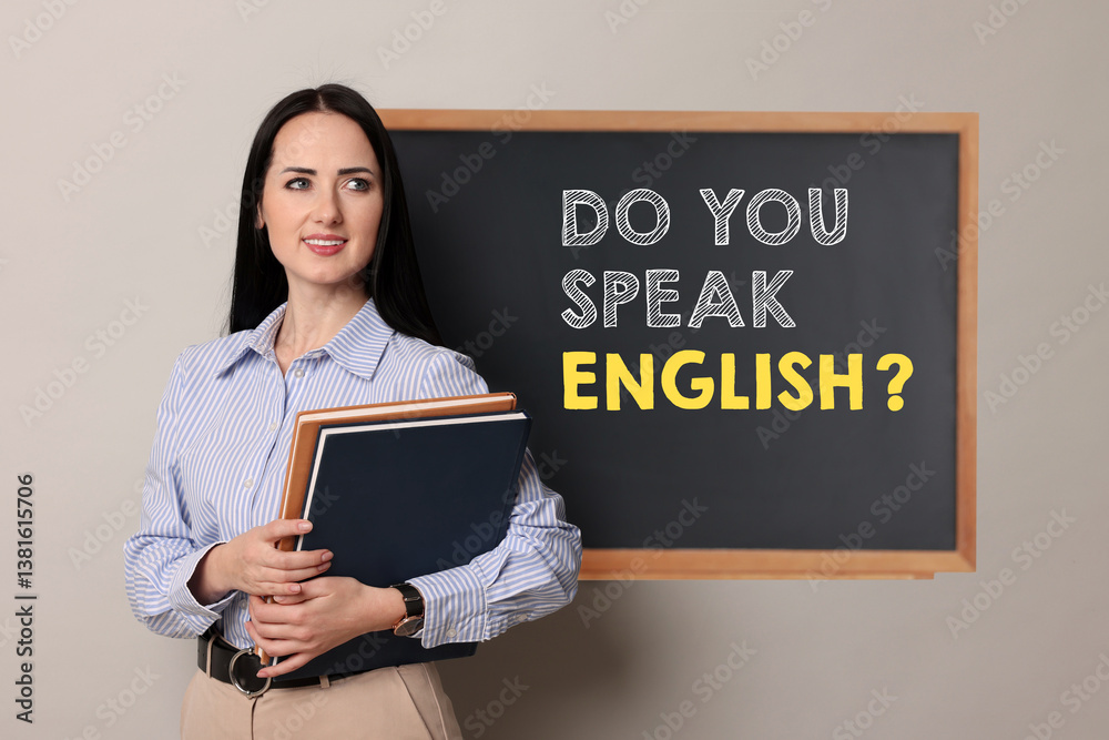 Teacher near black chalkboard with phrase Do You Speak English? in classroom Teacher near black chalkboard with phrase Do You Speak English? in classroom