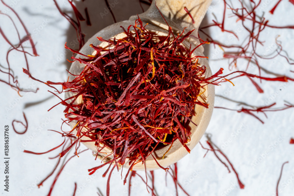 Naklejka premium red Saffron threads in wood spoon spilling on white marble background, light and airy with sunlight and shadows, top down view
