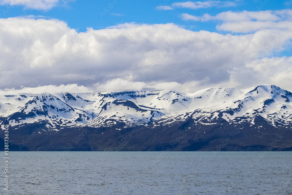 Fototapeta premium Snowy mountains reflecting in the Iceland sea under cloudy sky