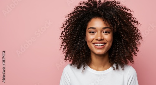 A smiling woman with beautiful curly hair poses against a soft pink background. Her bright smile radiates joy and positivity, making it an ideal image for beauty or lifestyle contexts.